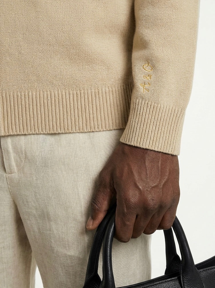 Person wearing a beige sweater with a brand logo, holding a black handbag.